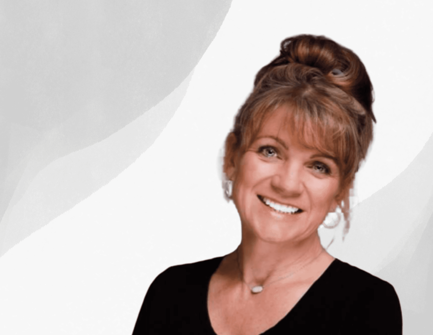 A smiling woman with light brown hair in a high bun, wearing a black top, hoop earrings, and a necklace, poses in front of a light gray and white abstract background.