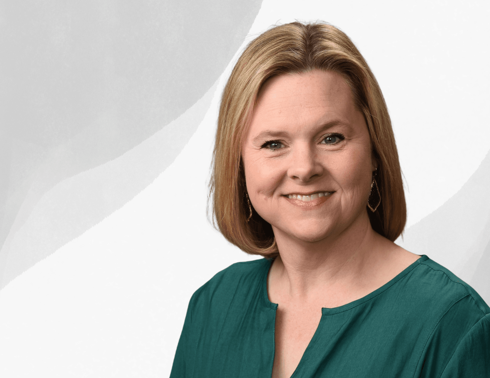 A woman with straight blonde hair wearing a green top and drop earrings smiles at the camera against a light, abstract background.