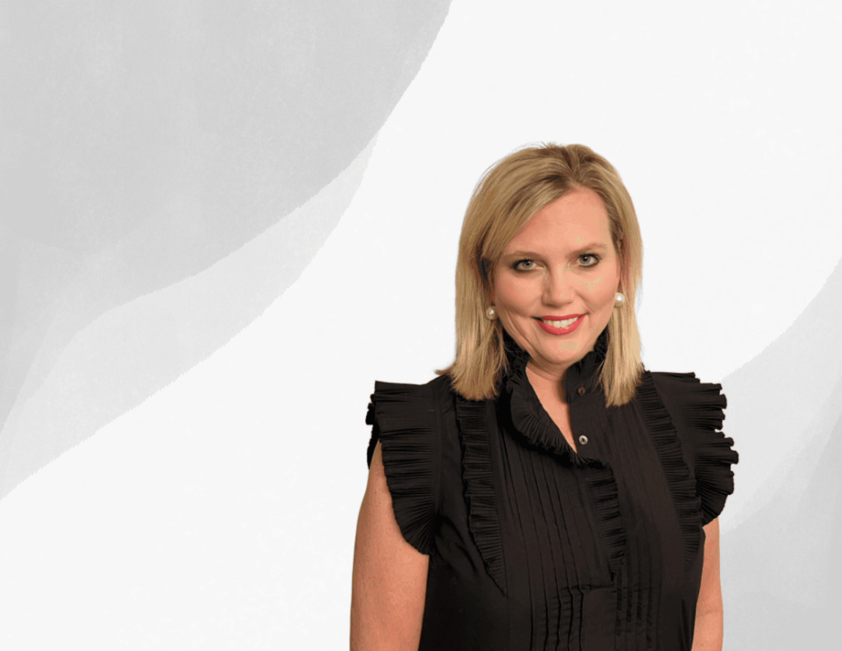 A blonde woman in a black, sleeveless, pleated top stands in front of a light gray abstract background, smiling at the camera.