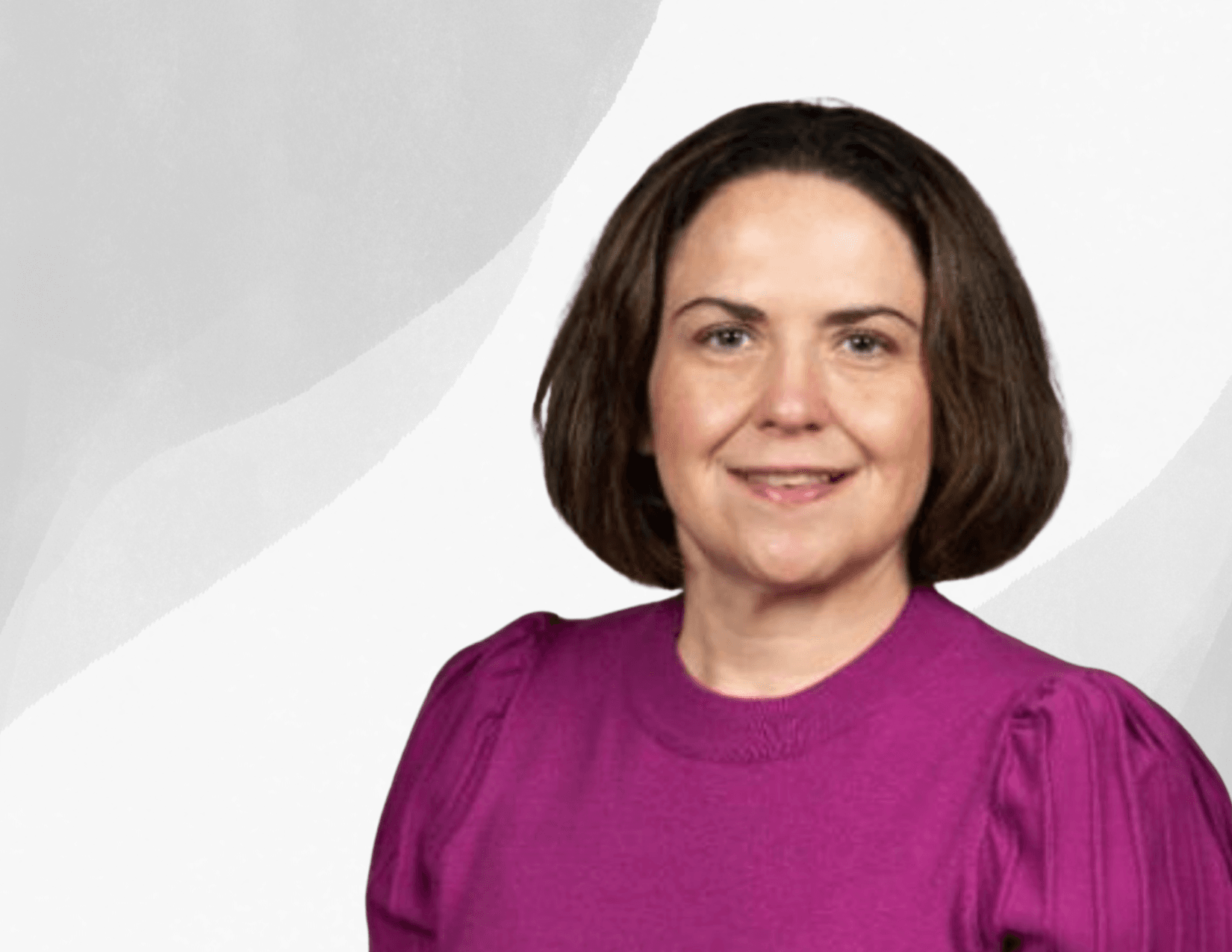 A woman with straight, shoulder-length brown hair is wearing a bright purple top and smiling in front of a light gray abstract background.
