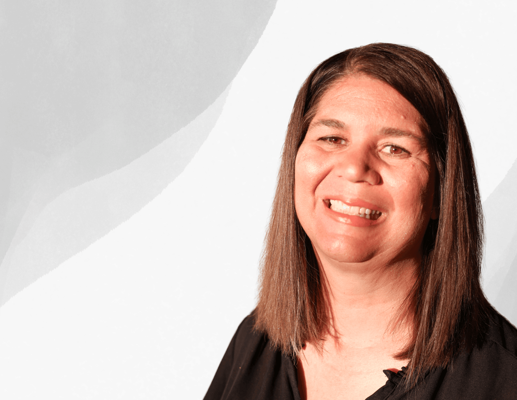 A woman with straight brown hair, wearing a black top, smiles at the camera against a light gray abstract background.